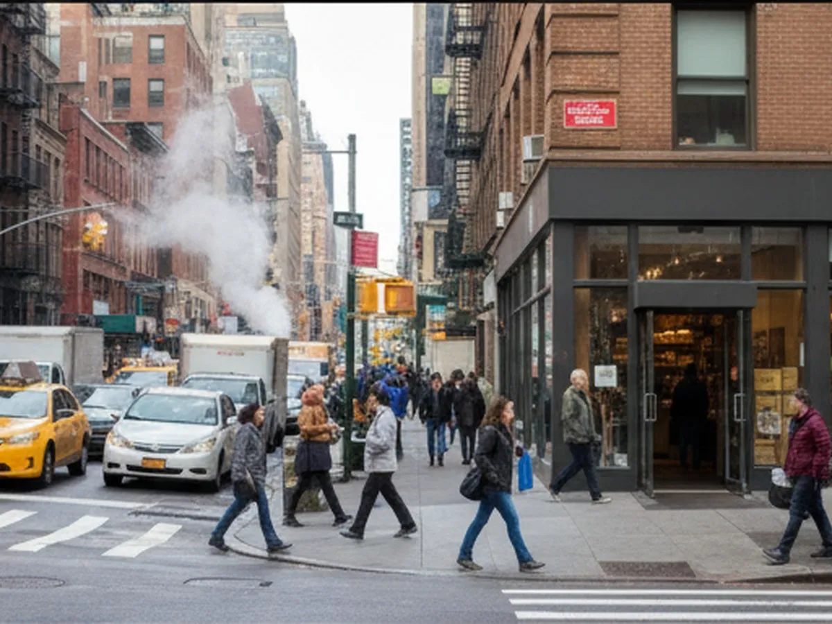 Sunlit street corner in Midtown Manhattan during morning rush hour, with typical NYC traffic, pedestrians in casual workwear, and a coffee shop entrance framed by classic brownstone and glass storefronts, steam rising from a subway grate, and soft reflections on nearby windows.