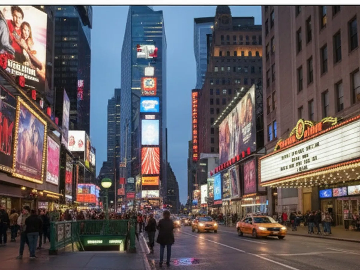 Twilight street scene in Times Square with bright movie billboards glowing above a line of people outside a multiplex, yellow cabs and subway entrance visible, photographed from eye level with natural lighting.
