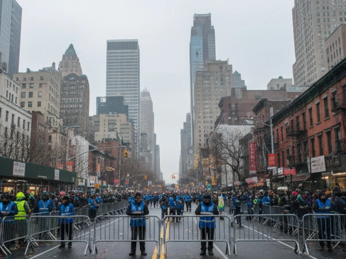 Wide-angle morning view of Manhattan streets as metal barricades line the sidewalks, volunteers in generic jackets set up crowd-control barriers, and early spectators in coats and hats gather under overcast skies, with midtown skyscrapers rising in the background and no readable signs or logos visible.
