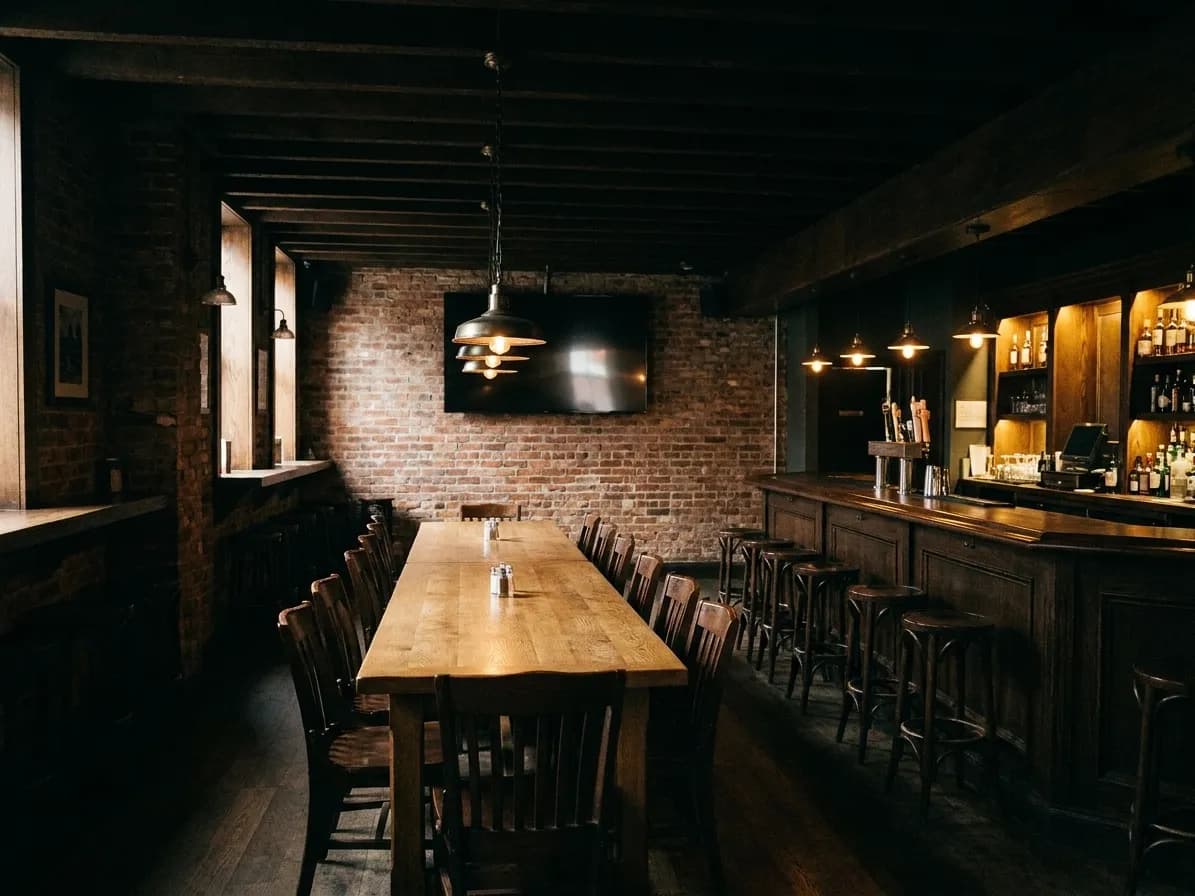 A private back room in a New York bar set up for a group, one long table down the middle, a large screen on the far wall, warm low lighting