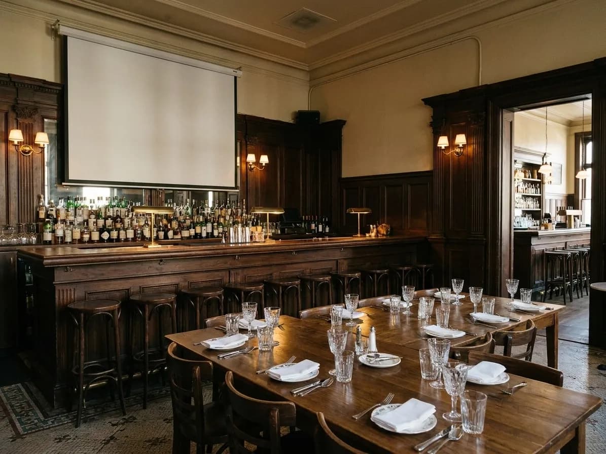 A wood-panelled San Francisco bar's side room with a long table, a projector screen pulled down at the end, glasses set out for a group