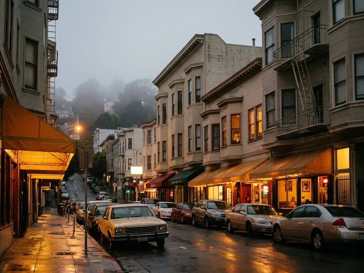 A narrow North Beach restaurant block in San Francisco at dusk, warm light from low storefronts reflecting off wet pavement