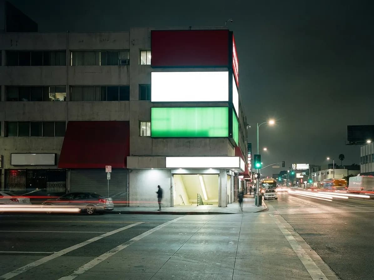 A Koreatown Los Angeles building at night, stacked illuminated signage panels up the facade, cars passing on a wide street below