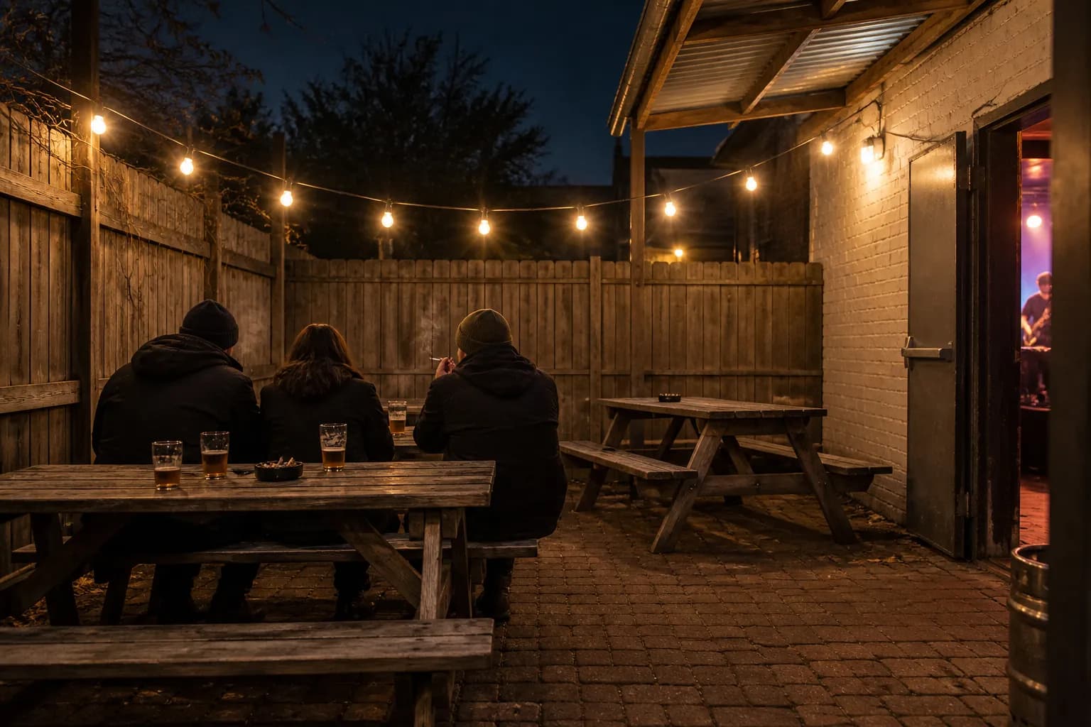 A small back patio behind a music venue with string lights and picnic benches
