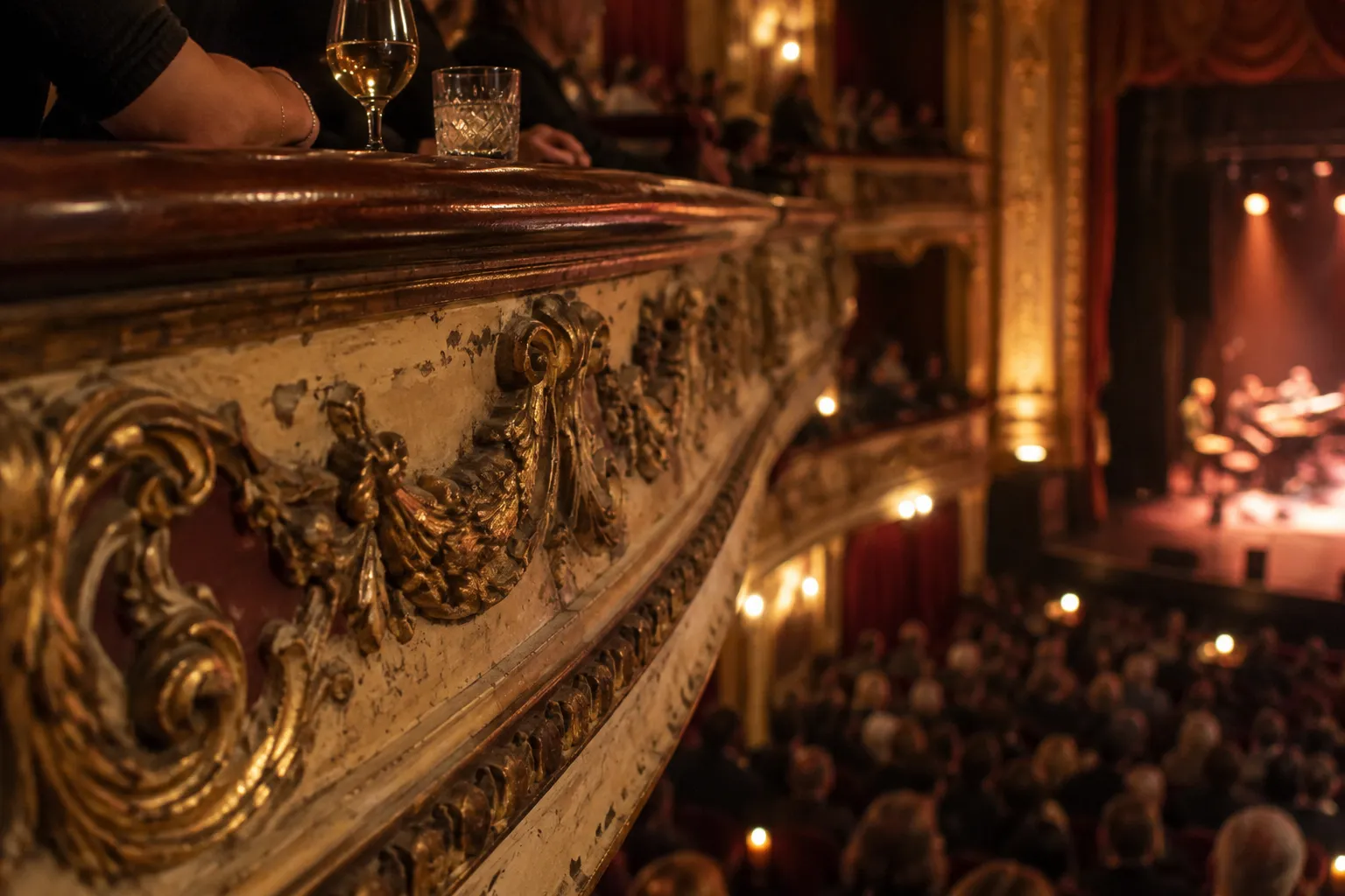 An ornate theatre balcony with carved columns and a gilded ceiling above a stage