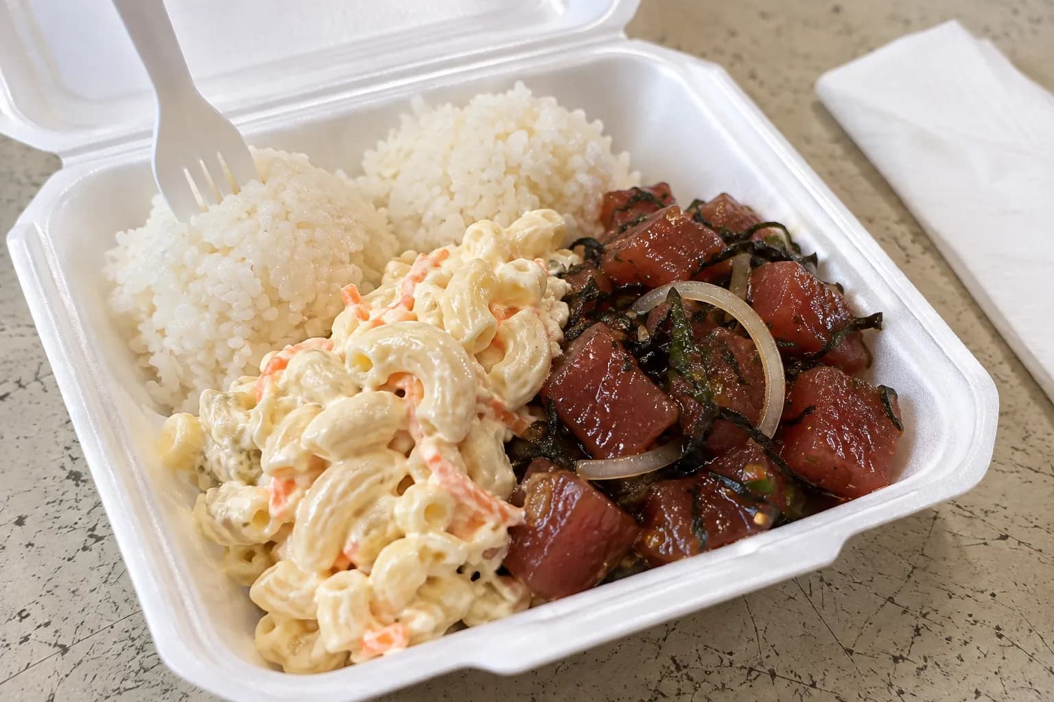 A takeaway plate of poke, white rice and macaroni salad in a paper container