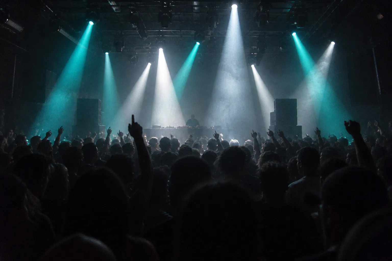 A crowded dance floor close to a low DJ booth under hard beams
