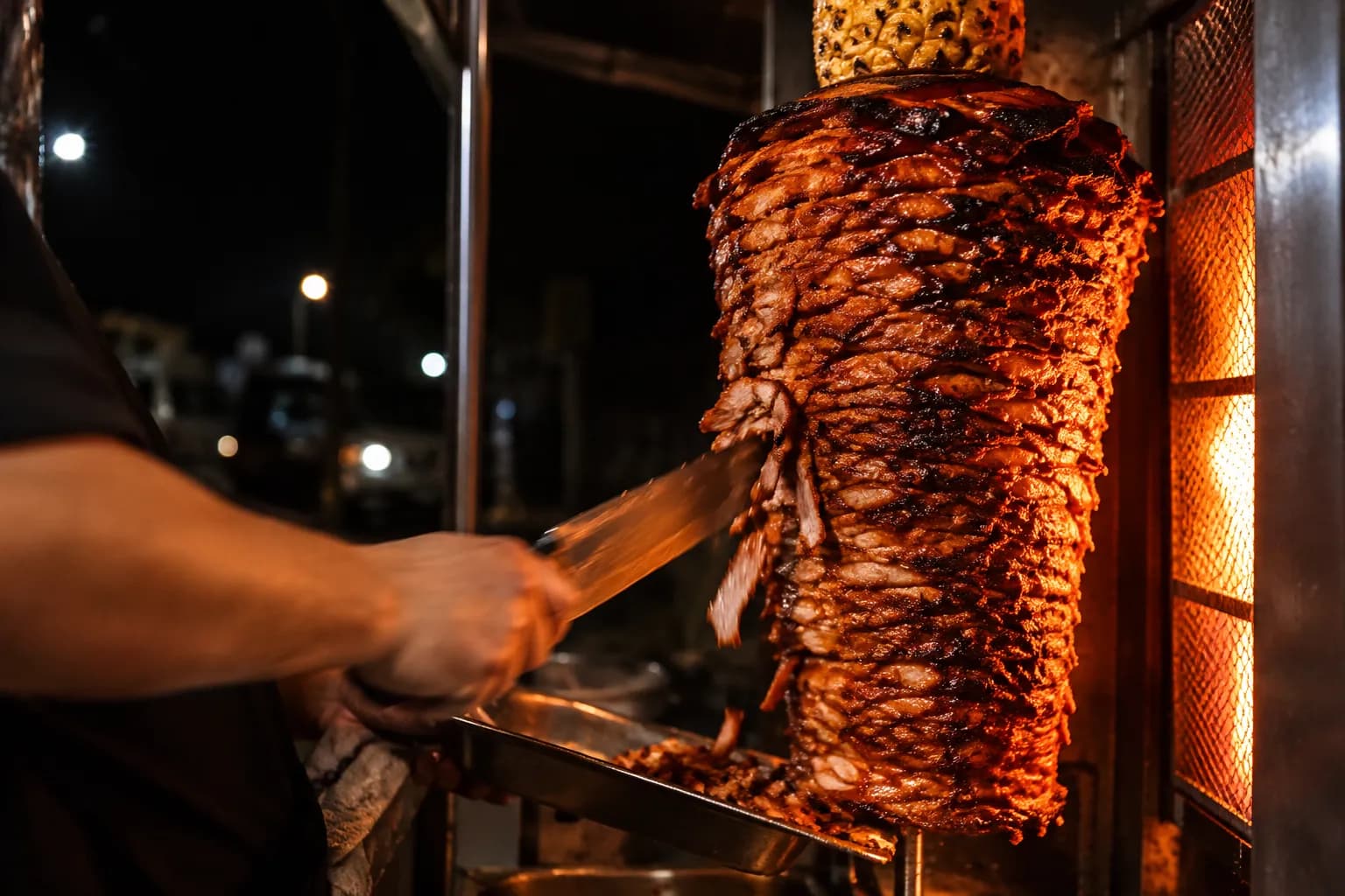 A vertical spit of marinated pork with a pineapple on top, glowing under a food truck light