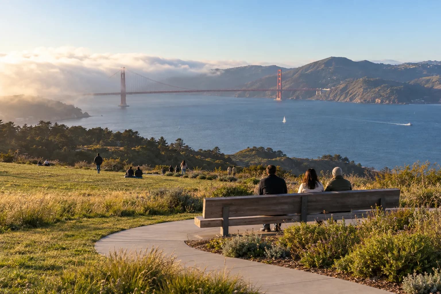A grassy park overlook with a view across a bay toward a red suspension bridge