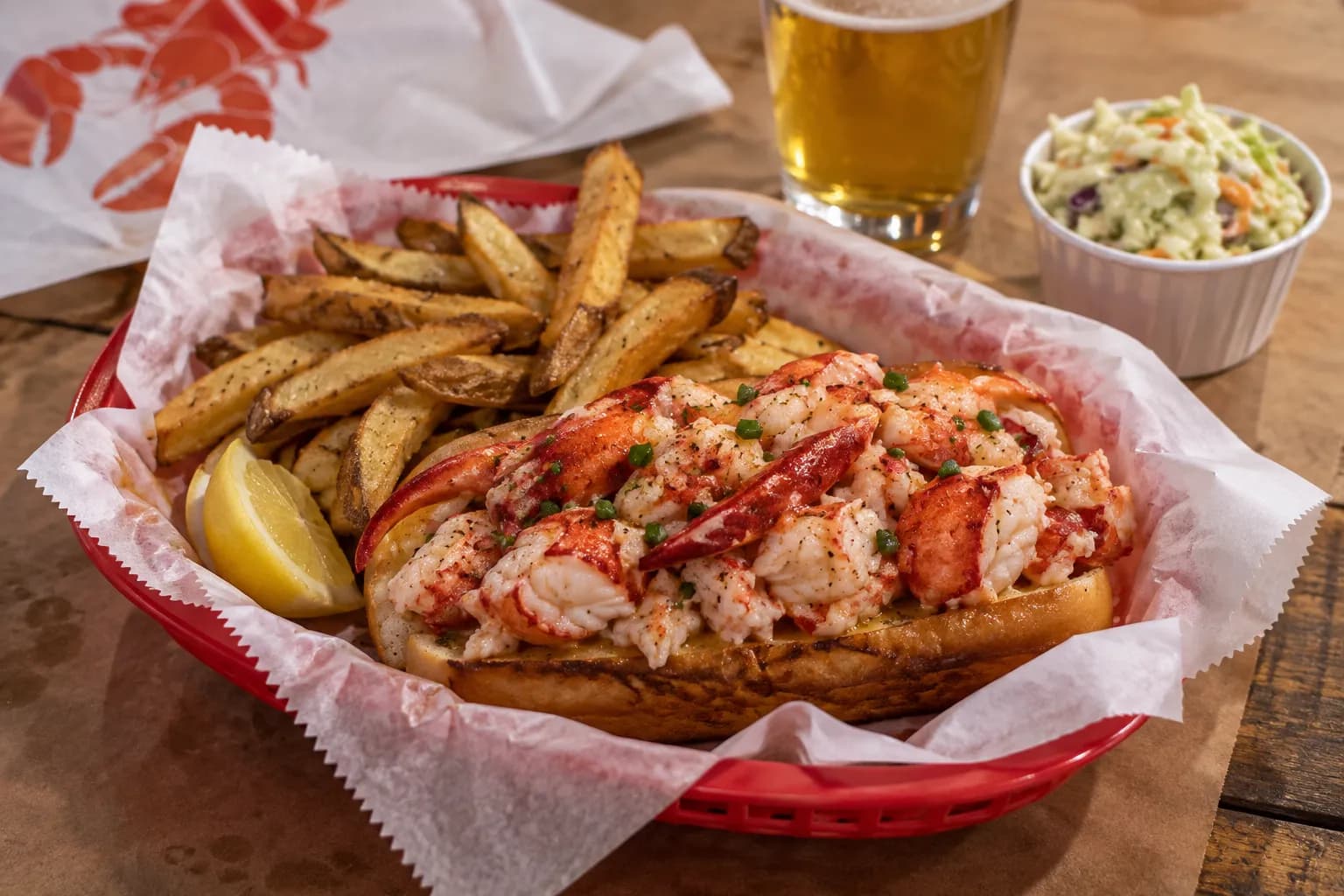 A lobster roll on a split bun with fries in a paper-lined basket