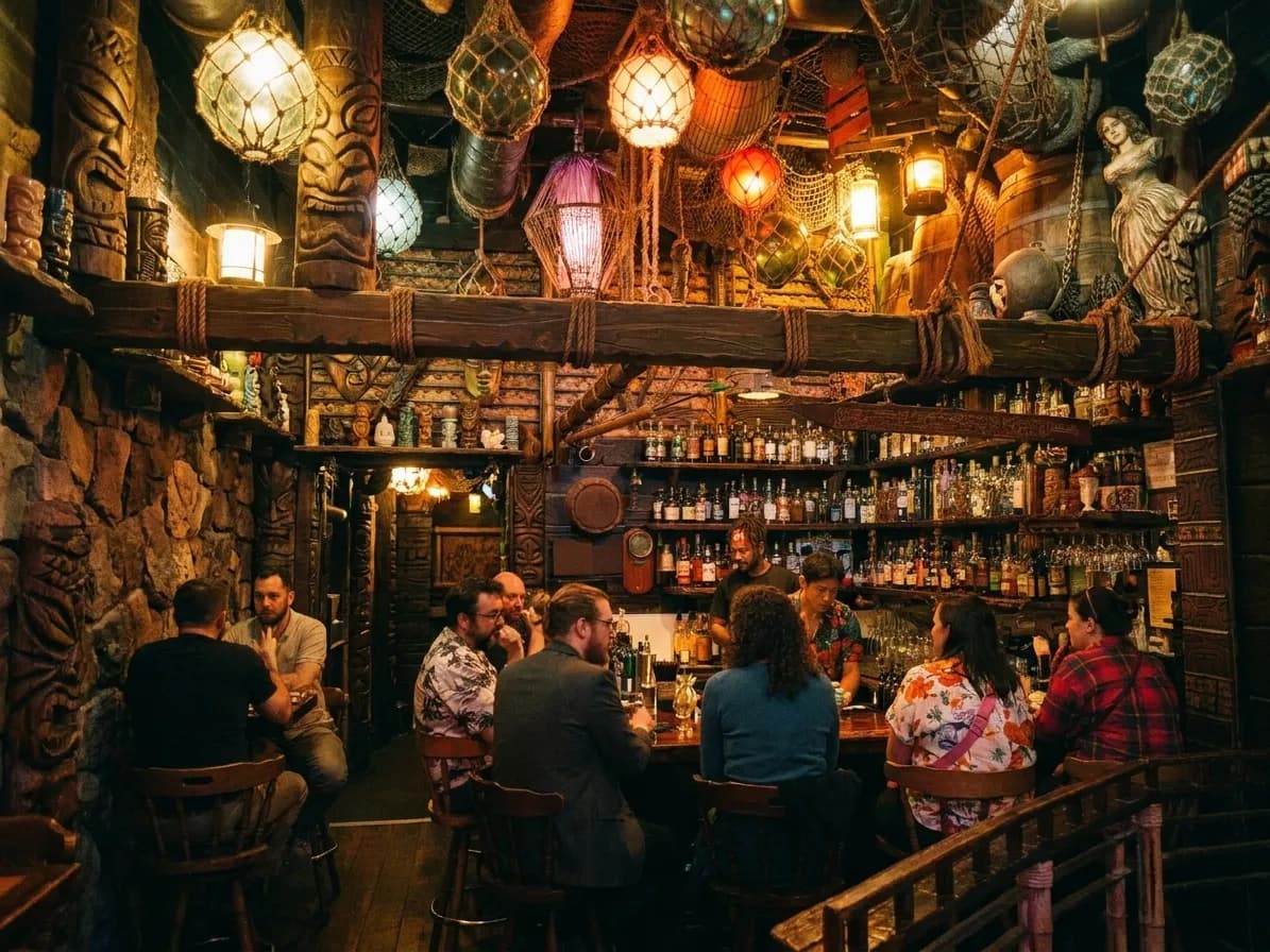 A dim tiki bar interior with carved wood, glass float lamps overhead and a crowded narrow bar