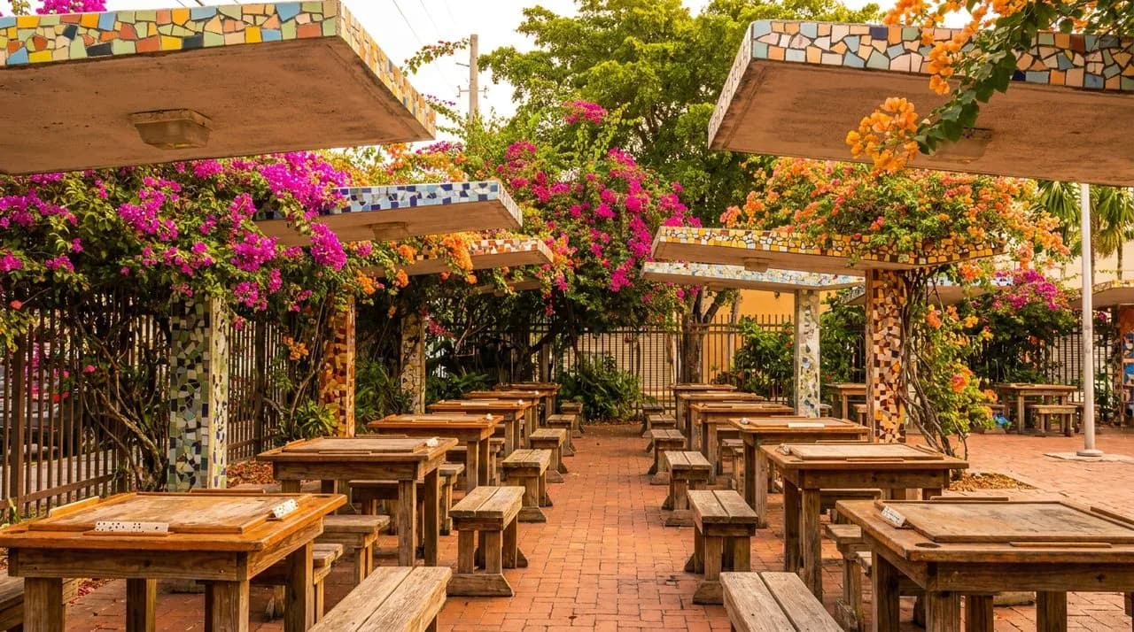 Maximo Gomez Domino Park in warm late morning light, with colorful tile mosaic awnings and empty domino tables.