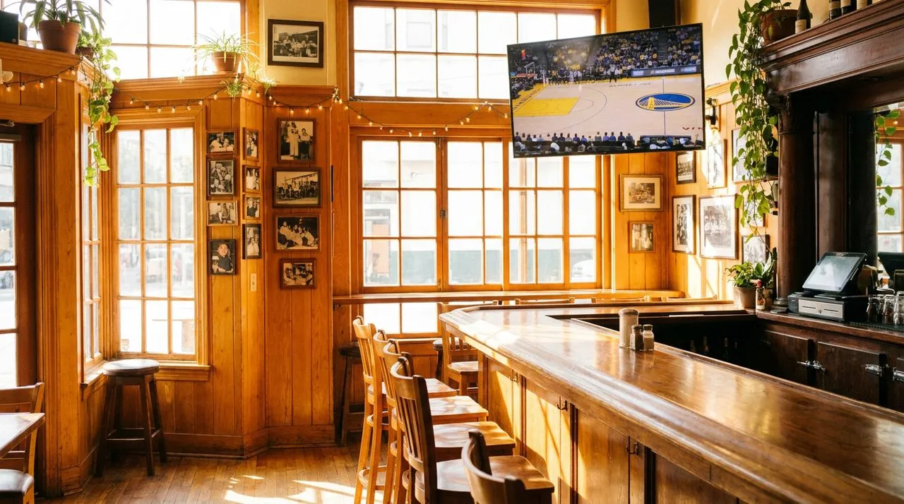 North Beach Italian-American bar interior with honey wood paneling, warm sunlight, polished bar counter, and mounted TV showing basketball.
