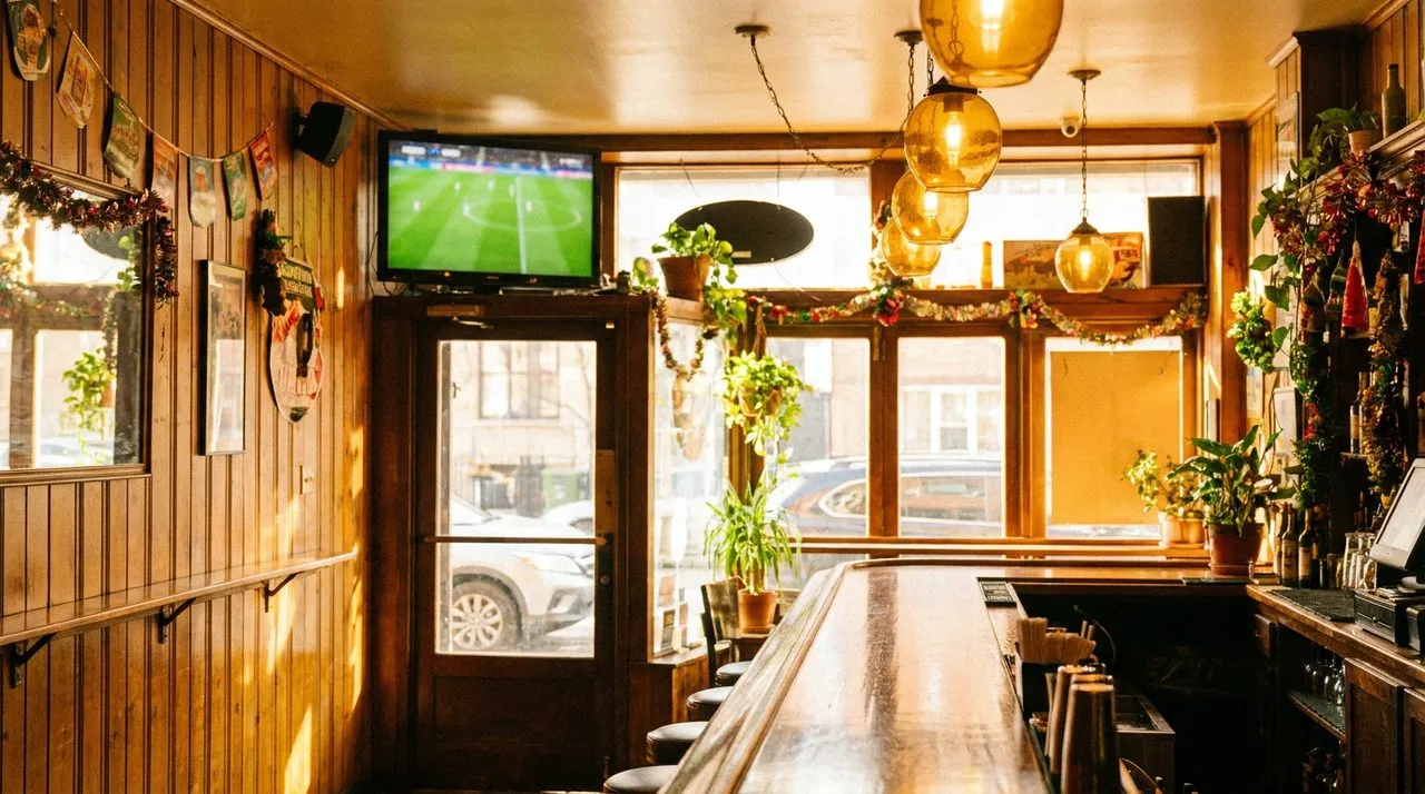 Greenpoint Polish-American bar interior on a bright afternoon, warm wooden bar, vintage amber glass pendant lights, retro wood paneling, mounted TV showing soccer pitch, festive neighborhood atmosphere.