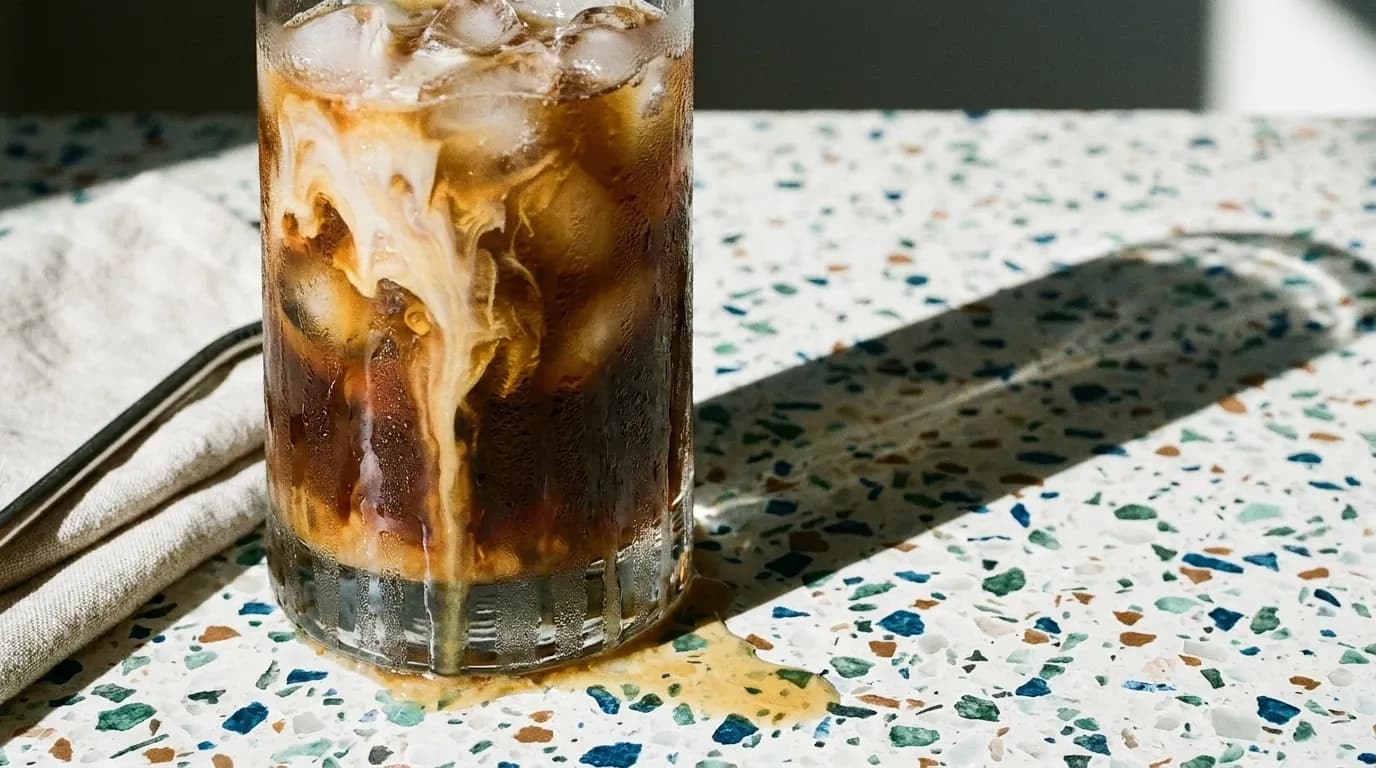 A tall glass of iced coffee with condensation on a stone counter
