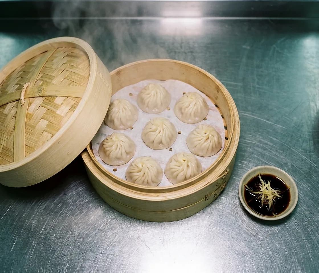 A bamboo steamer basket open on a counter with folded dumplings inside