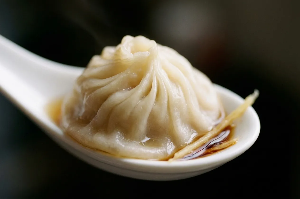 A single pleated soup dumpling lifted on a flat spoon