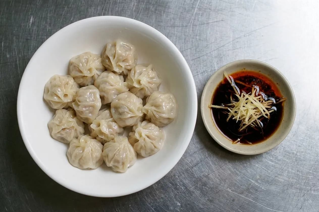 A bowl of boiled dumplings beside a saucer of dark vinegar and chilli oil