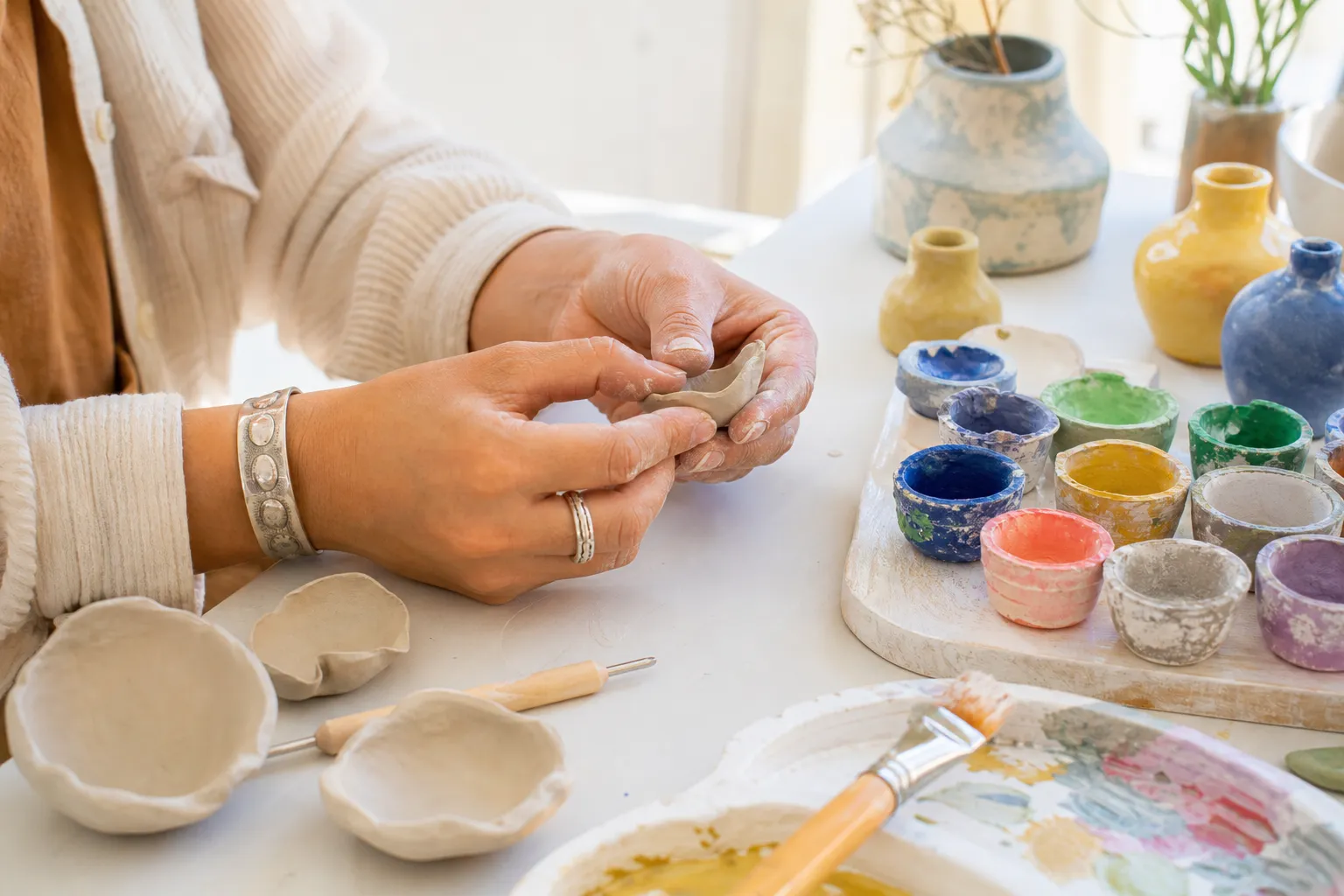 Bright close-up of hands shaping clay and arranging colorful workshop materials