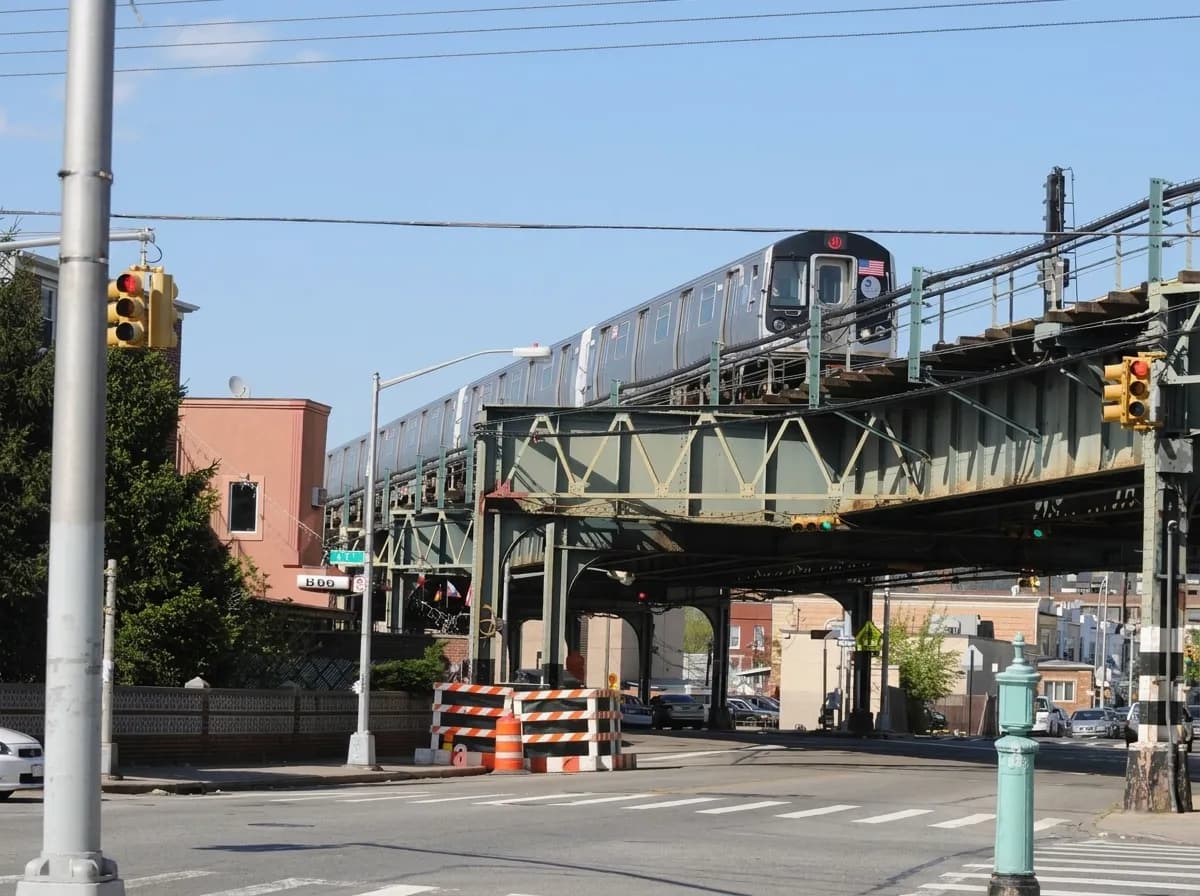 Elevated subway train crossing above a Brooklyn avenue on green steel tracks near Bensonhurst