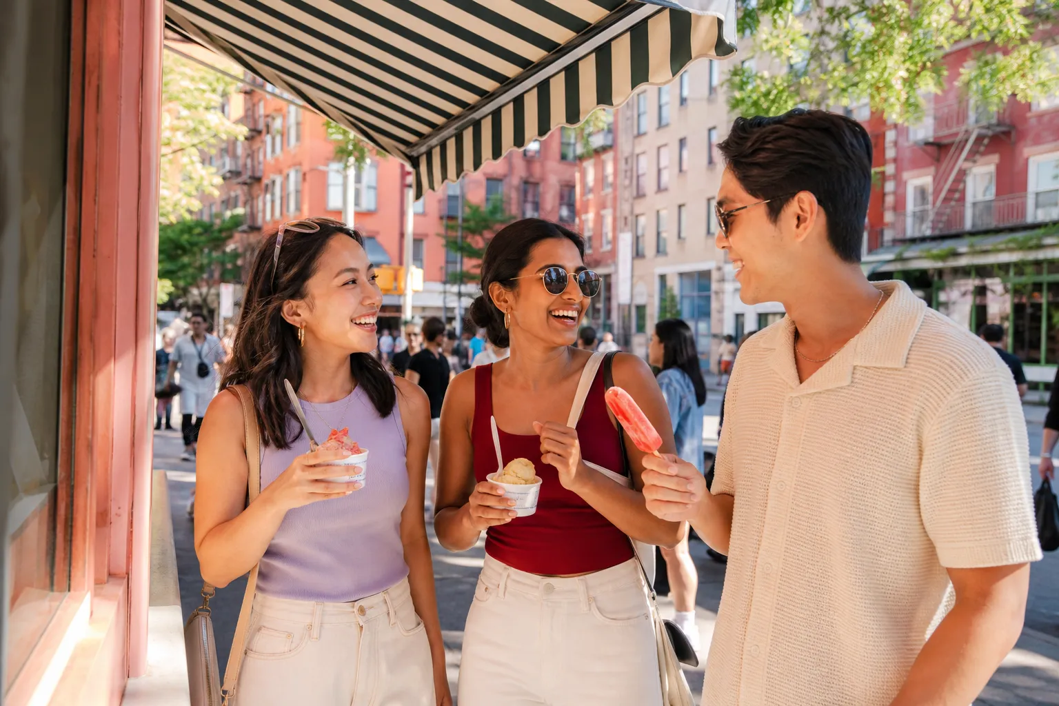 A sunny NYC sidewalk dessert stop with people holding colorful cold treats