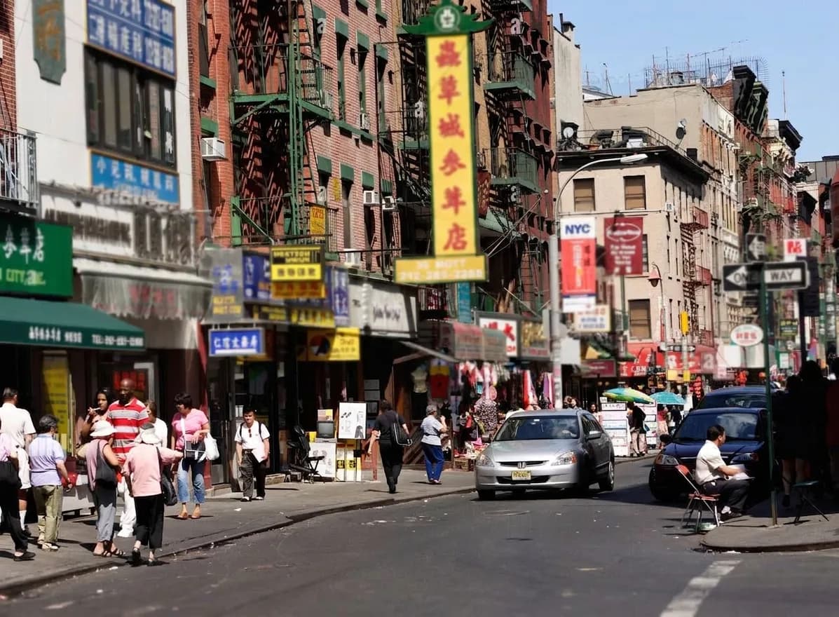Sunny Chinatown street in Manhattan with fire escapes, hanging signs, and pedestrians near the subway