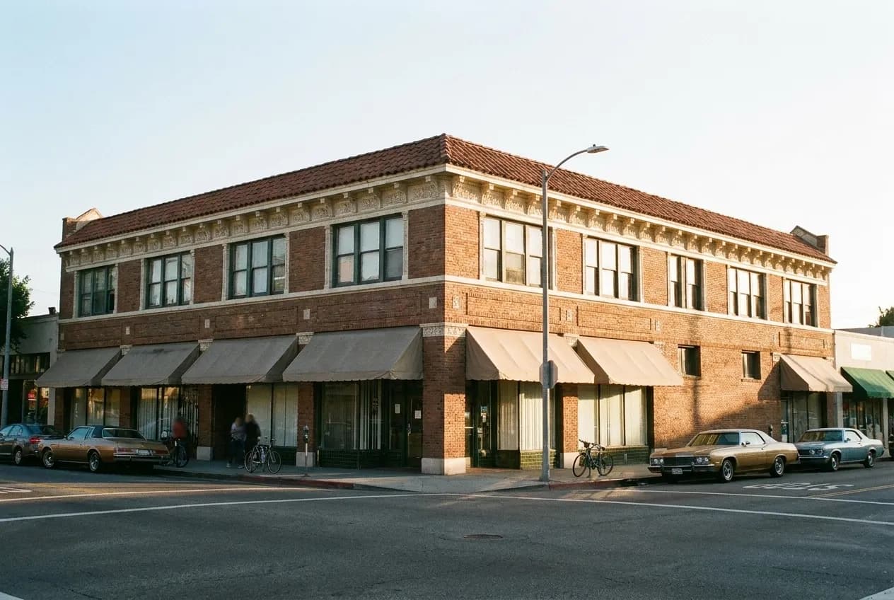 A two-storey brick commercial corner building with cloth awnings on a Highland Park boulevard in Los Angeles