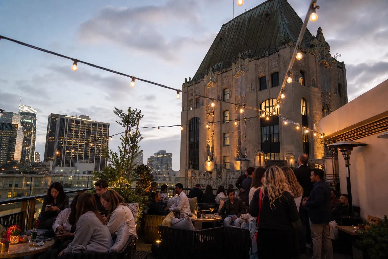 Patrons drinking at the open-air rooftop bar at Perch LA surrounded by historic skyscrapers.