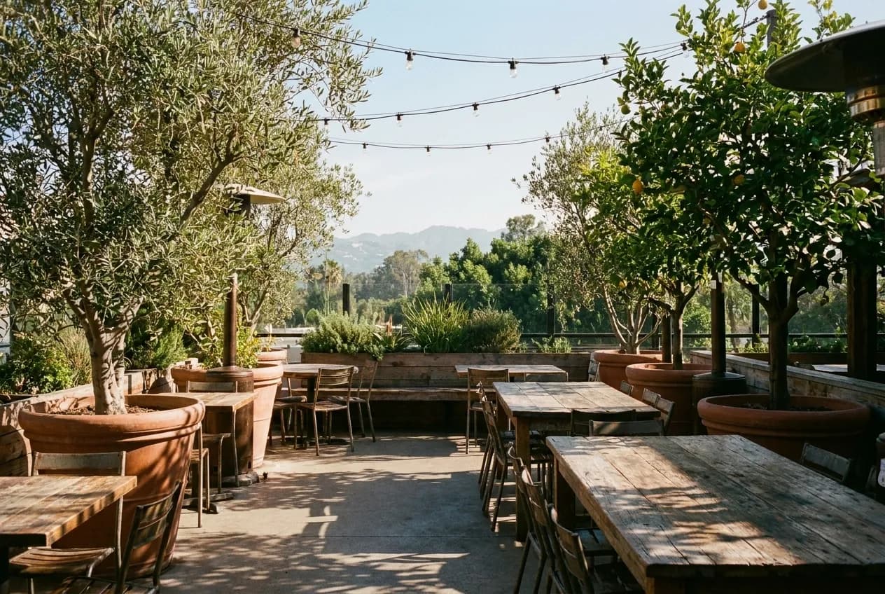 Empty garden patio with string lights and wooden tables overlooking Los Angeles hills in morning light at West Hollywood restaurant.