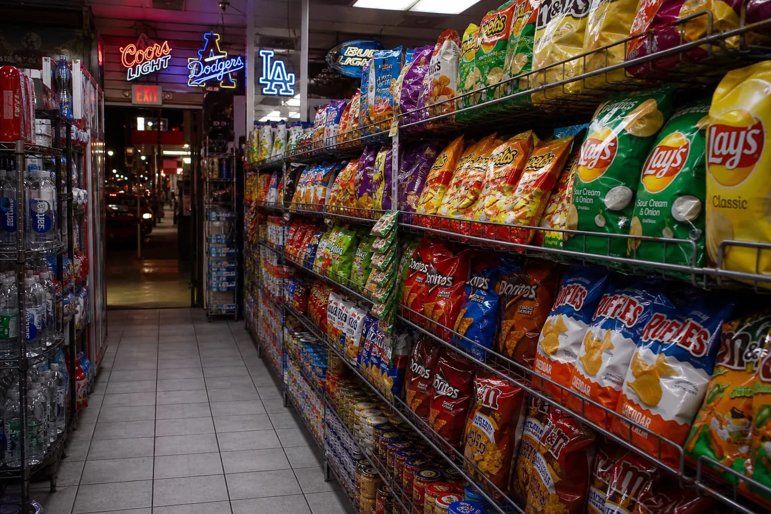 A brightly lit convenience store snack aisle in Los Angeles with colorful chip bags lining the shelves under neon lights.