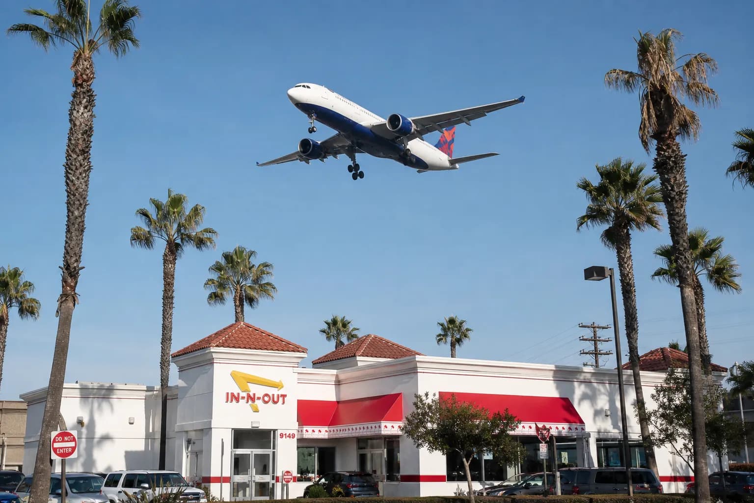 An In-N-Out Burger location in Westchester, Los Angeles under a blue sky with a commercial airplane flying low overhead.