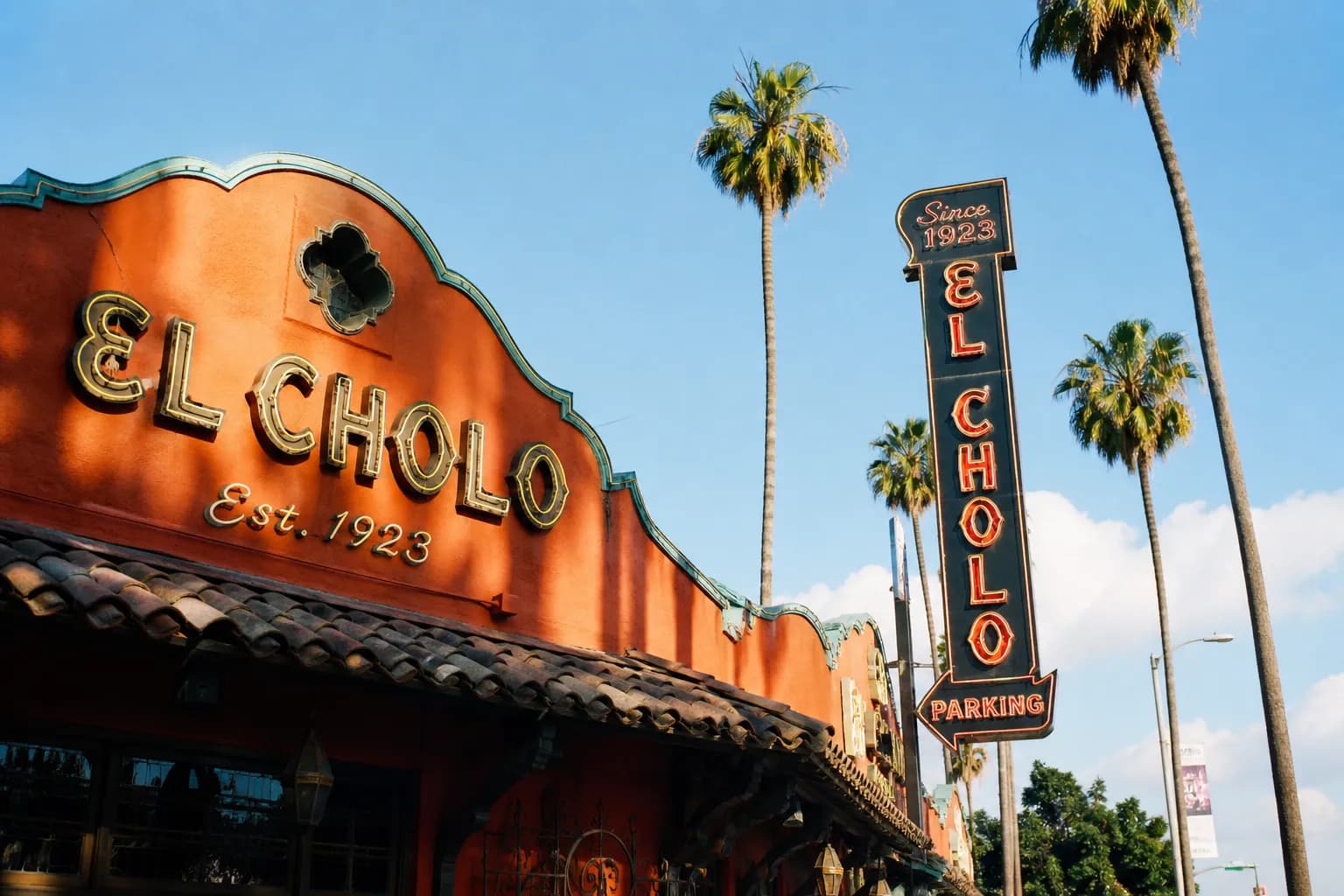 The exterior of El Cholo restaurant on Wilshire Boulevard with vintage signage and palm trees.
