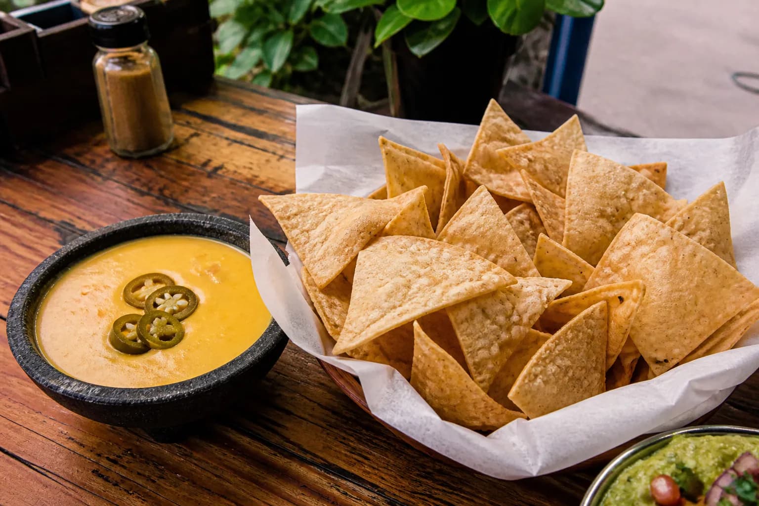 A bowl of warm queso dip topped with jalapeños surrounded by tortilla chips.