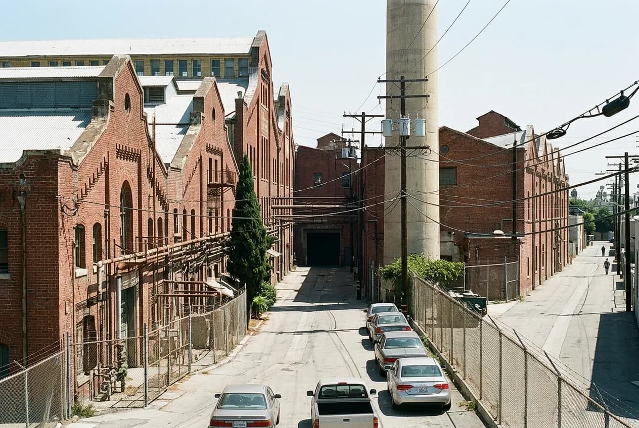 Brick industrial complex facade with a narrow alley entrance in Los Angeles's Arts District at midday.
