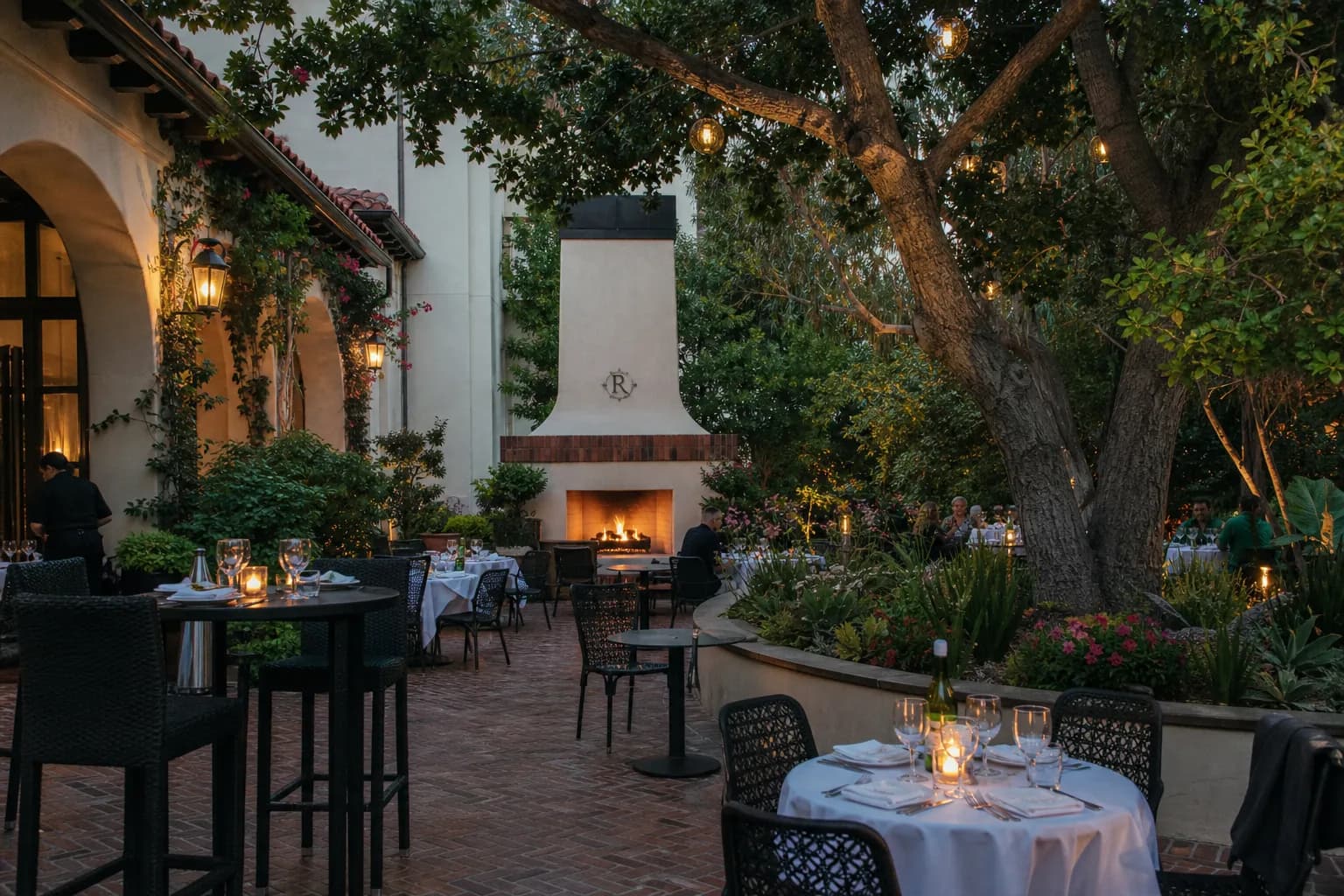 A romantic, foliage-draped outdoor brick patio with a lit fireplace at The Raymond 1886 in Pasadena.