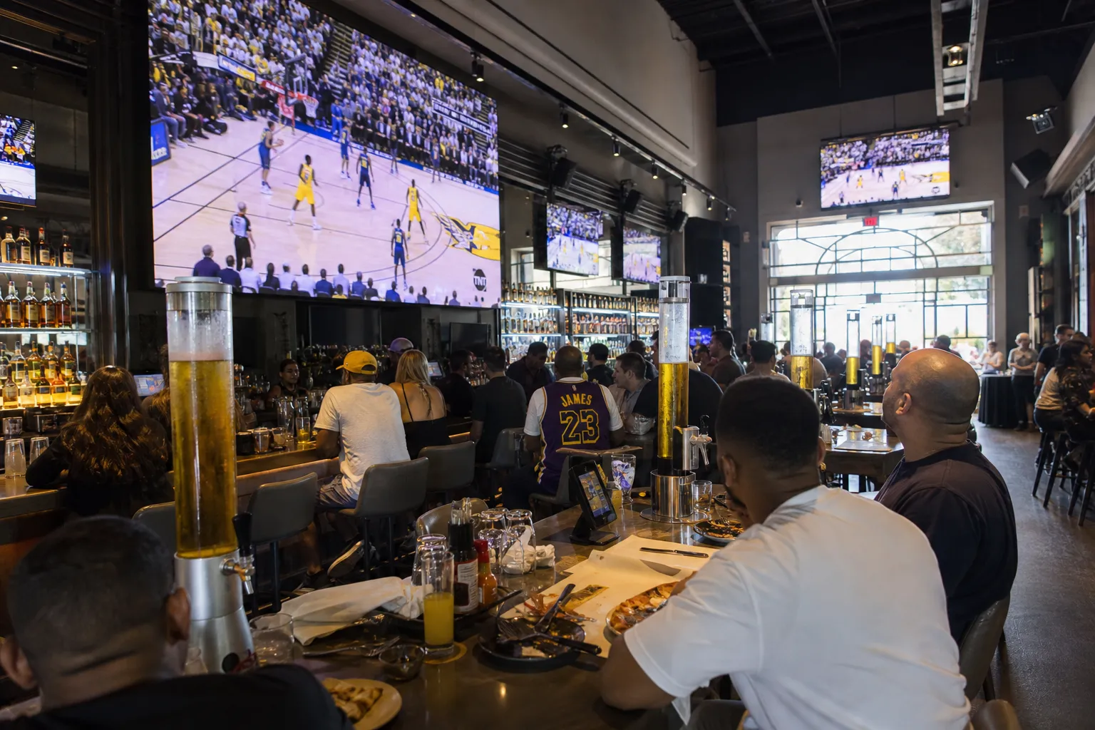 A spacious sports bar in Hollywood featuring giant screens, high-top seating, and people watching a live game.