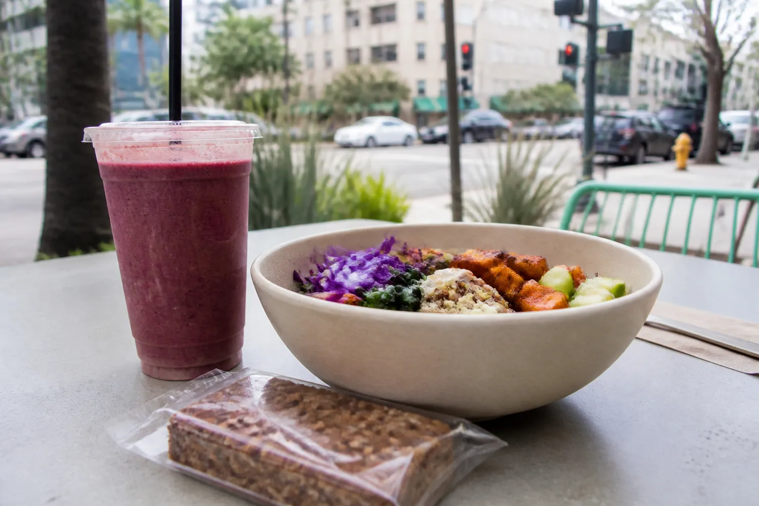 Smoothie, grain bowl, and packaged snack on an outdoor Los Angeles table
