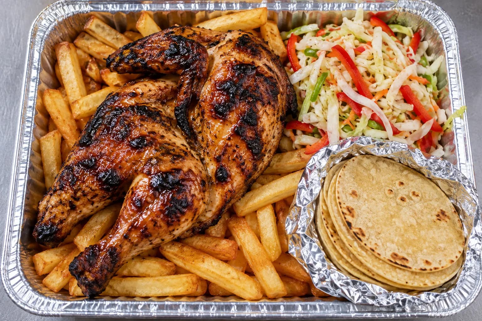 Char-grilled chicken laid over a bed of fries with slaw and tortillas beside it