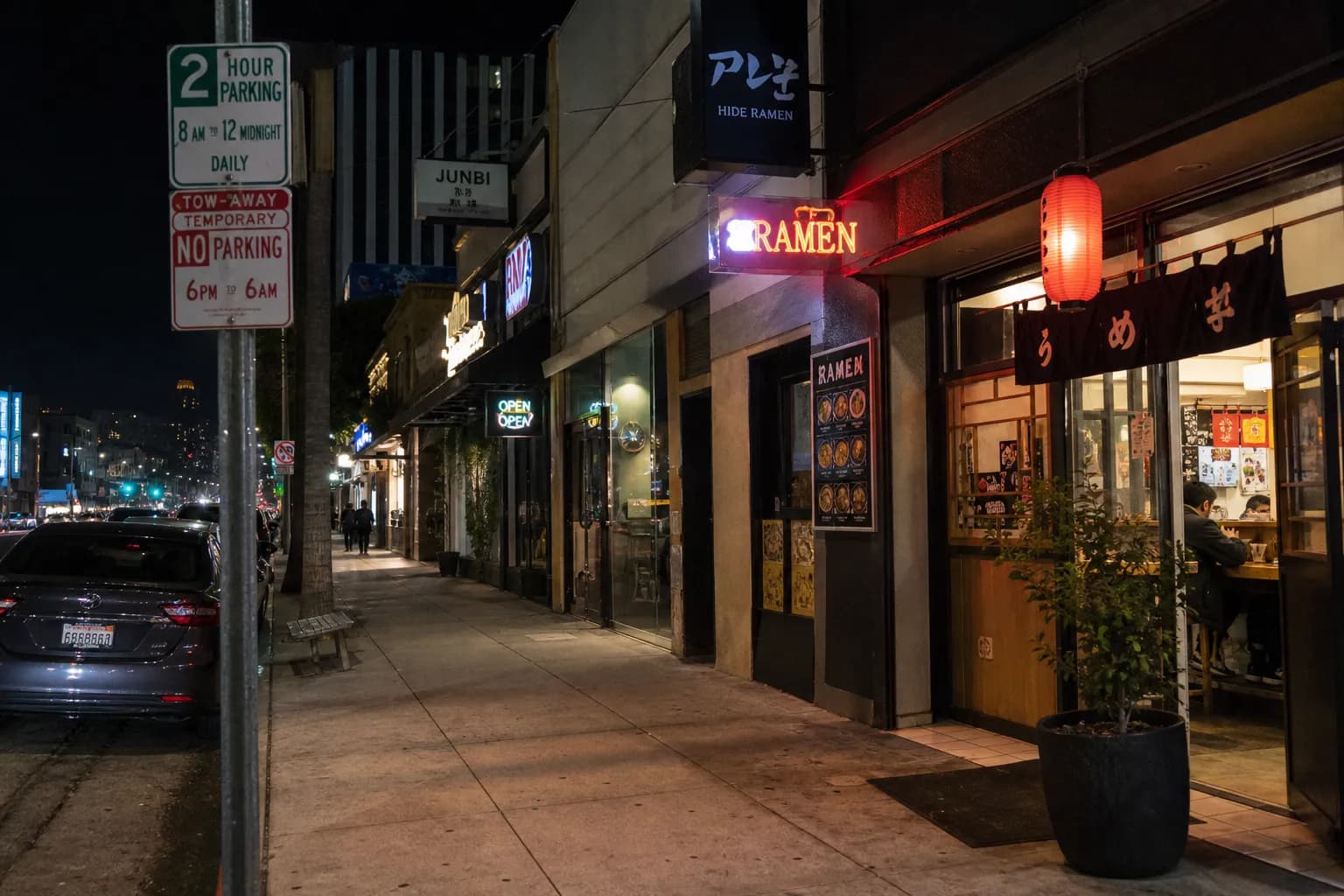 Street-level night view of a Koreatown ramen block in Los Angeles with glowing storefronts and parking signs