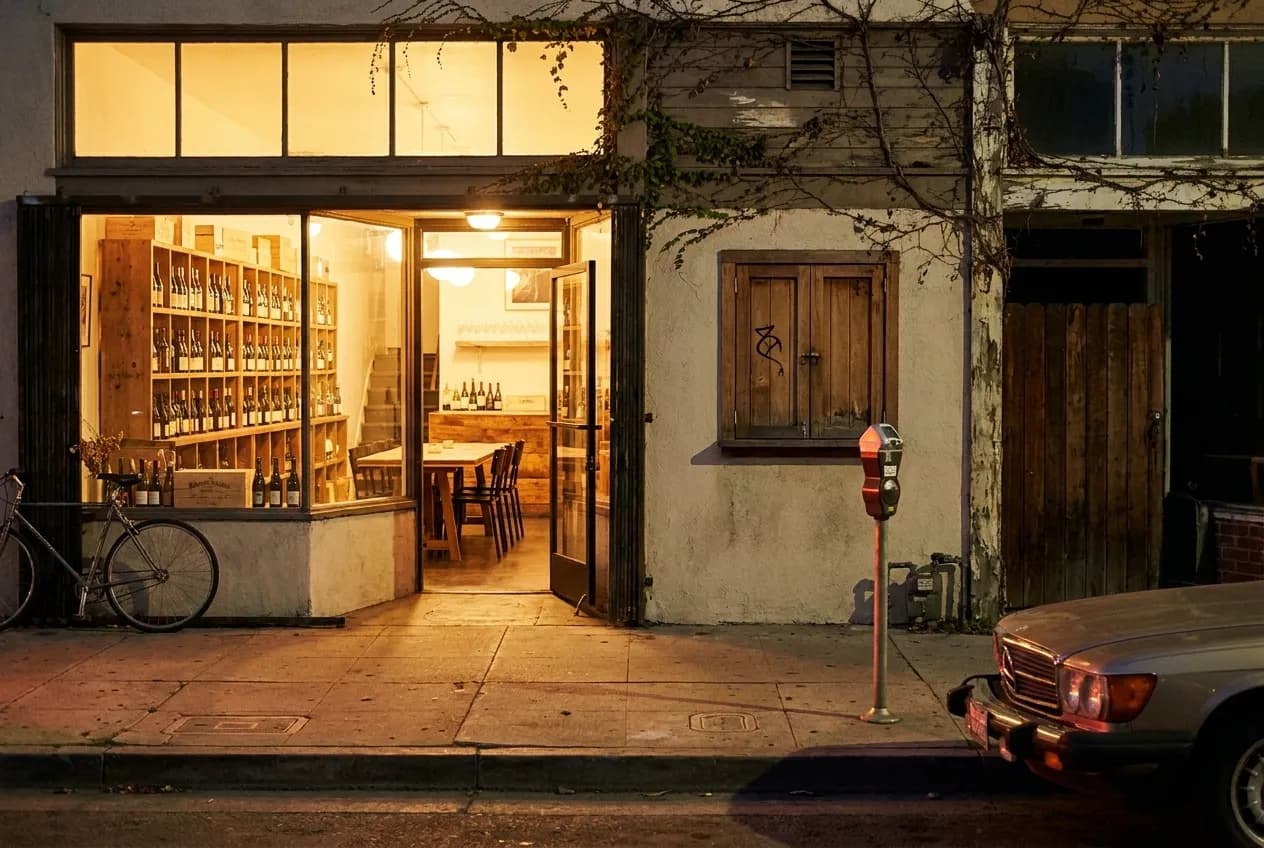 Vinovore wine shop exterior on Hoover Street at night with interior lights glowing through windows and bicycle leaning against storefront