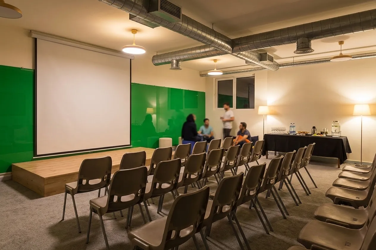 A coworking space set up for an evening event with rows of stacking chairs facing a low platform holding a blank projection screen
