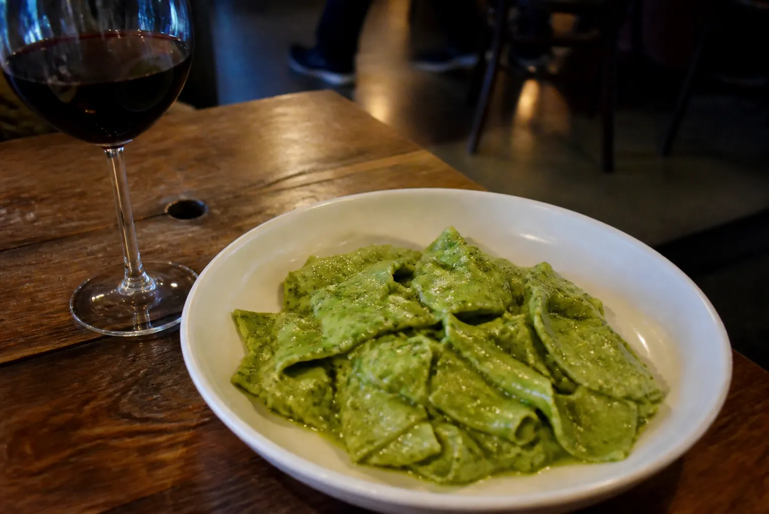 A close-up tabletop shot of a plate of fresh hand-rolled pasta, a glass of red wine, and warm ambient restaurant lighting in Downtown Los Angeles