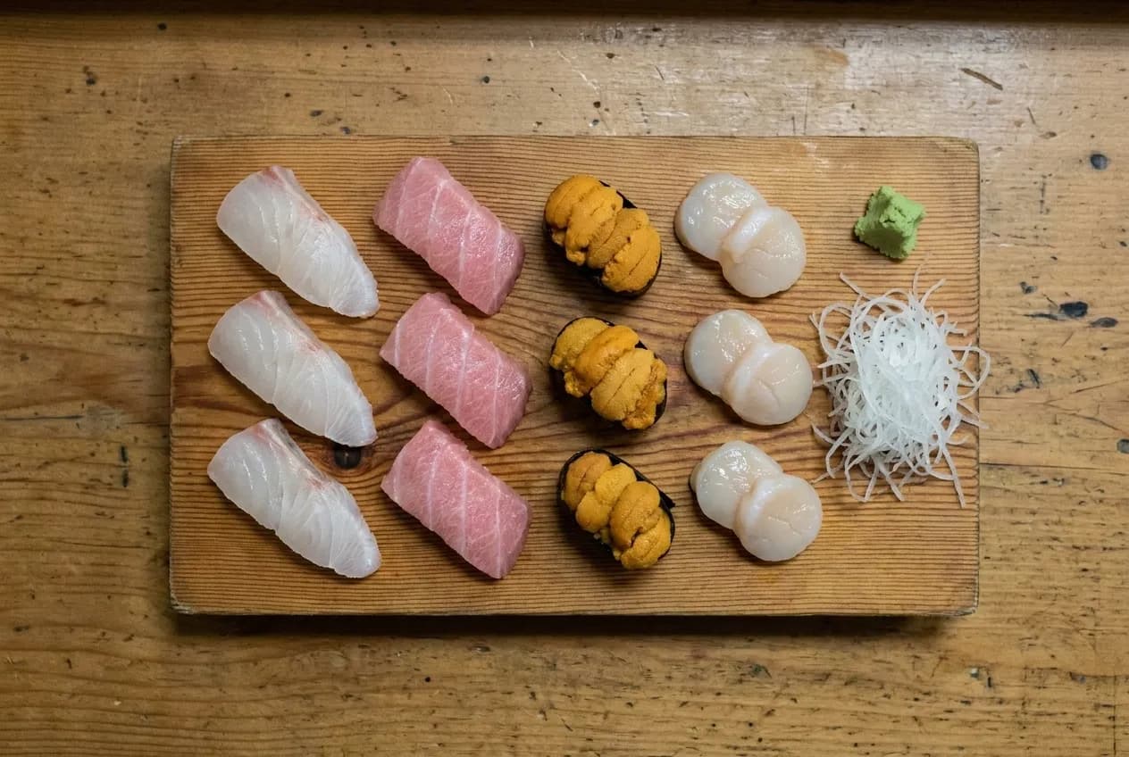 Sashimi deluxe platter on wooden board showing halibut, chutoro, sea urchin, scallop, wasabi and daikon from above.