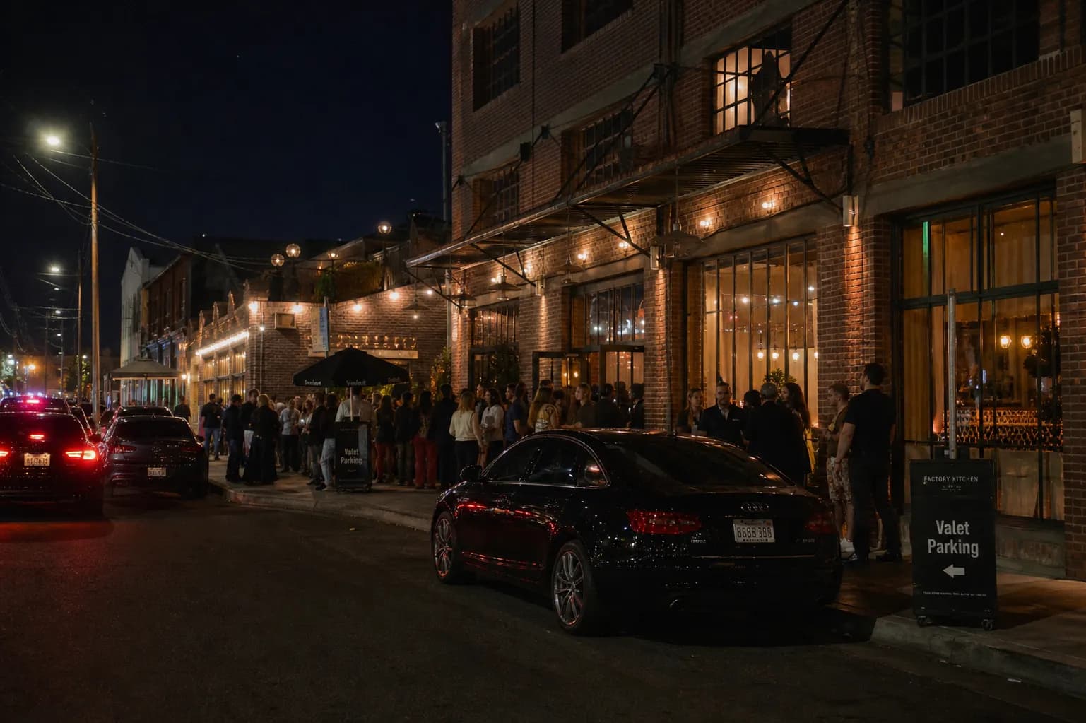 A bustling evening scene outside a trendy brick restaurant in the Arts District of Downtown Los Angeles, with warm string lights glowing overhead.