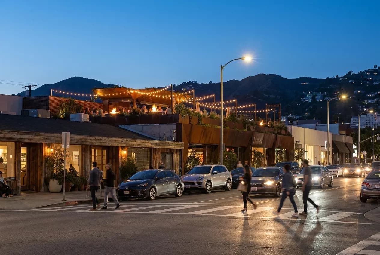 La Cienega Boulevard at dusk with illuminated rooftop terrace visible above street level, Hollywood Hills in background, pedestrians crossing street.