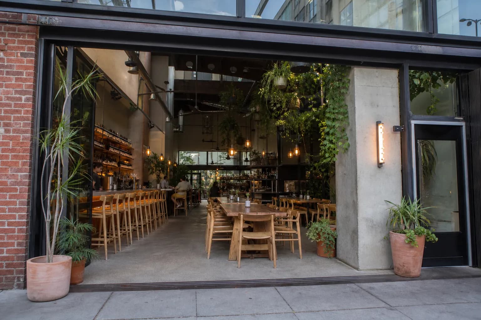 The stylish glass and steel storefront of a modern Downtown Los Angeles wine bar at dusk, with warm lighting glowing from within