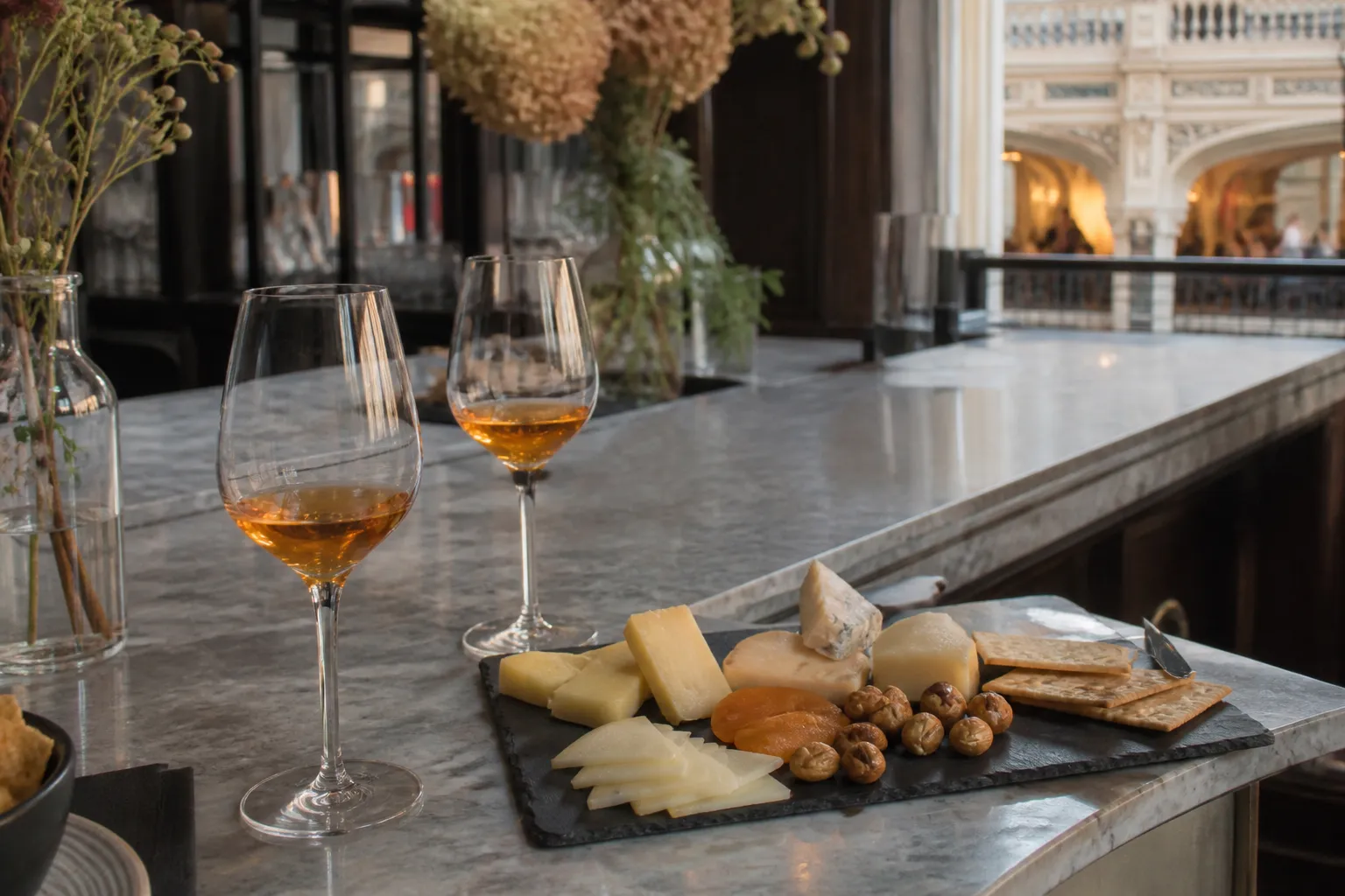 Two glasses of orange wine and a cheese board resting on a white marble bar counter in a chic Downtown LA arcade