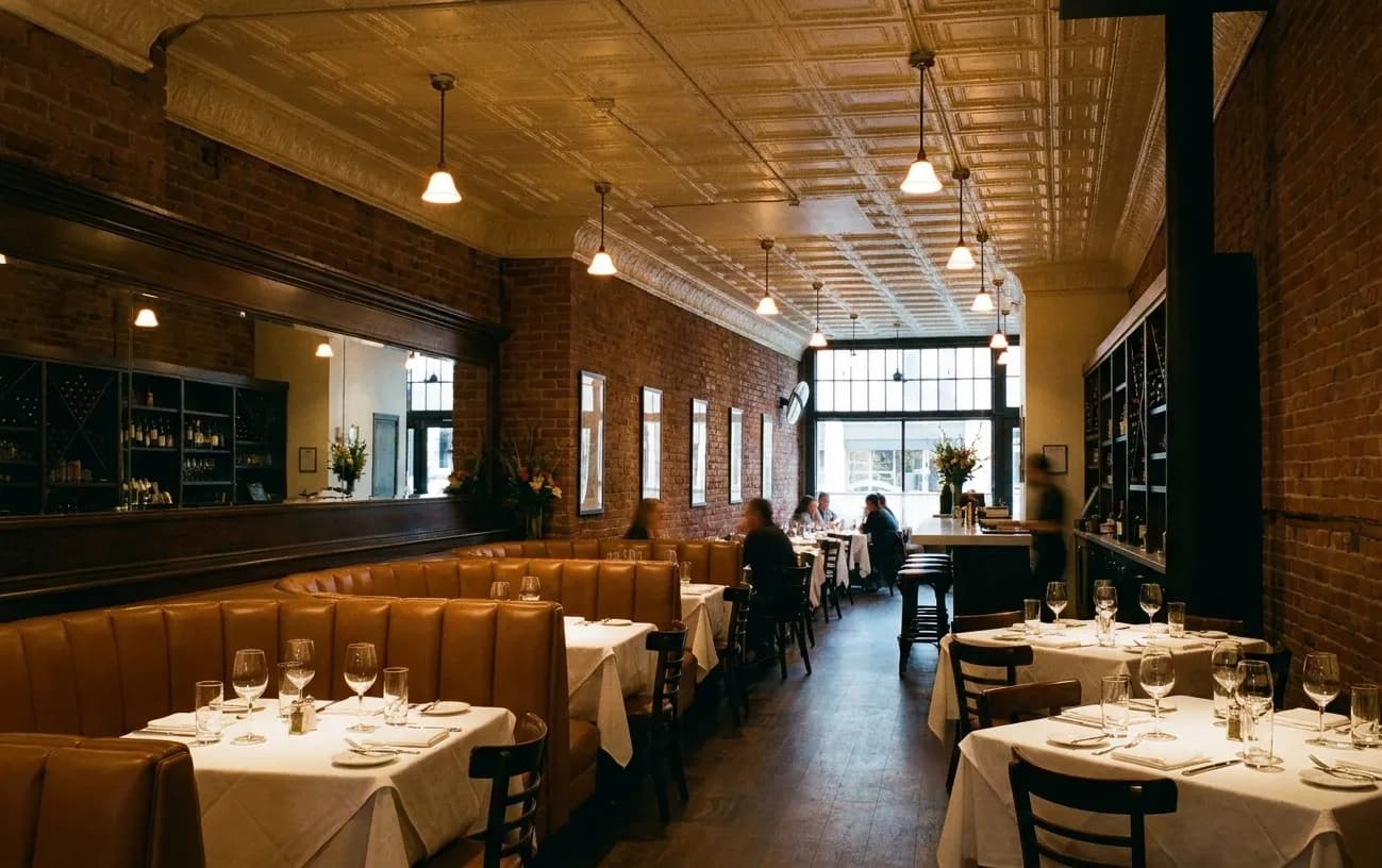An upscale Los Angeles dining room in the evening with caramel leather banquettes, small pendant lamps and tables set with white linen