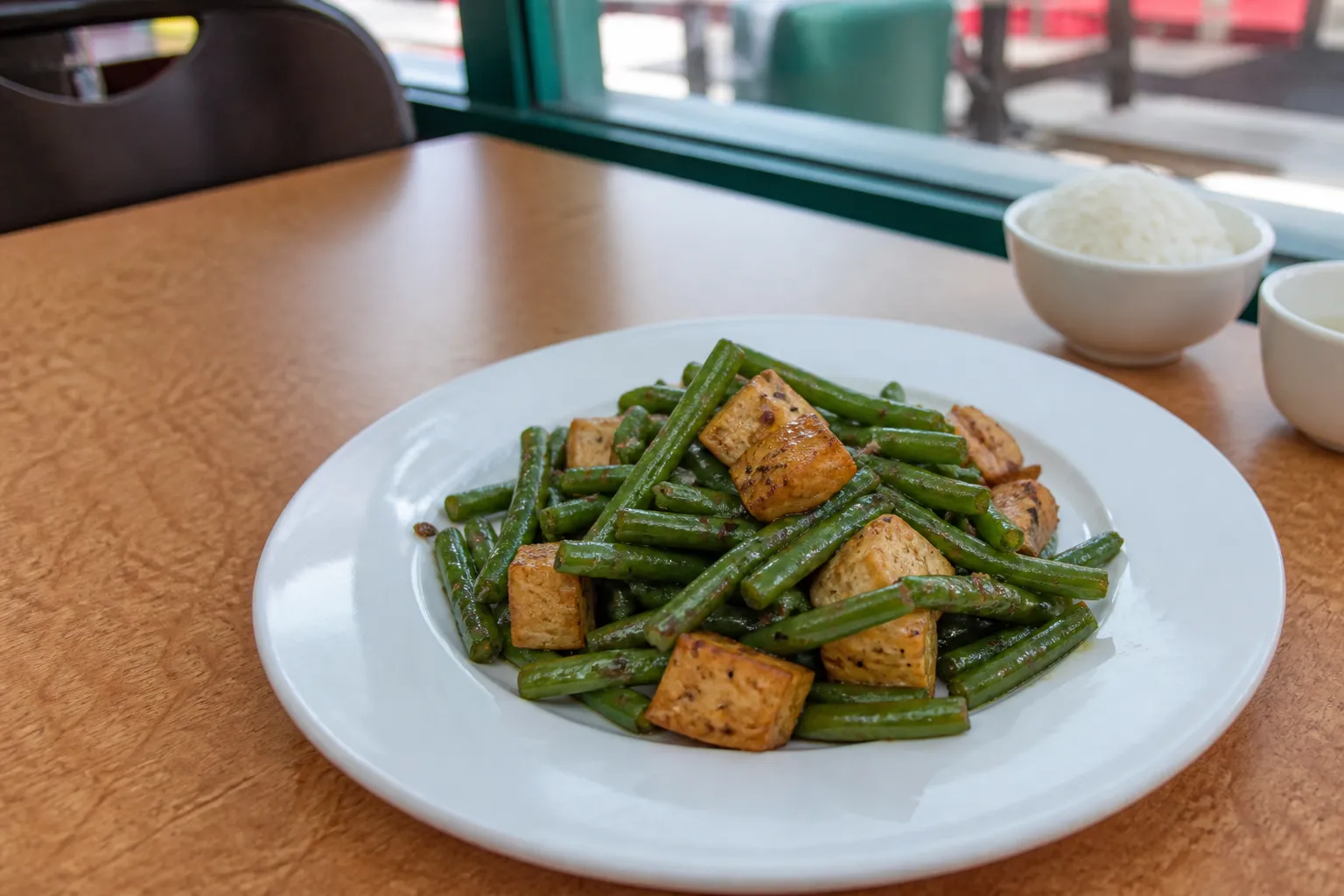 Wok-seared green beans and garlic tofu on a white plate in a Chinatown restaurant.
