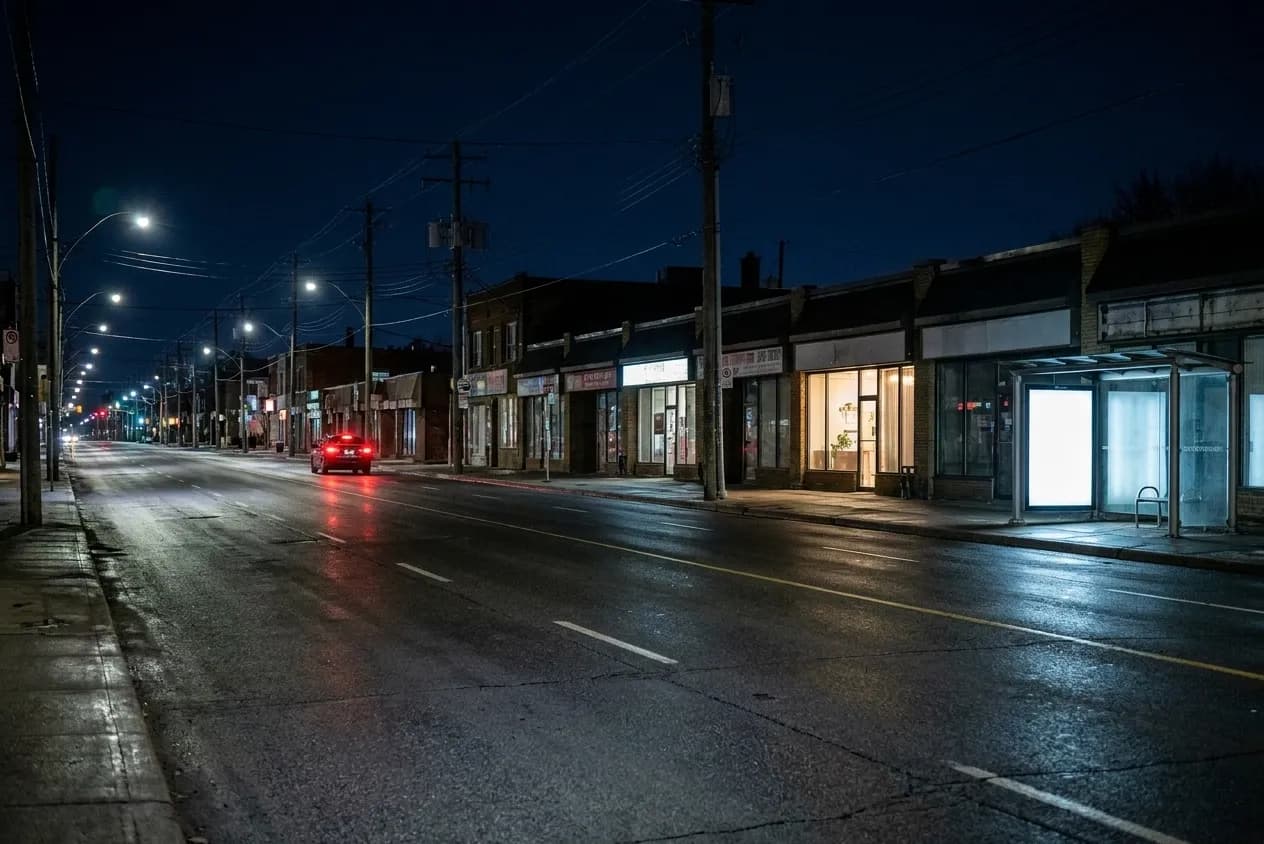 A wide Los Angeles boulevard late at night with two lit storefronts, a bus shelter and power lines overhead